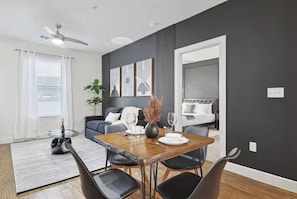 A modern living room with a dining area, a grey sofa, a coffee table, and a ceiling fan. - Chic and Stylish 2B near Legacy West  (Frisco)