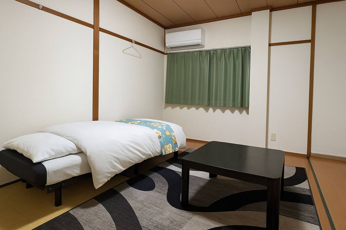 Ein kleines Zimmer mit einem Bett, einem Tisch und einem Fenster mit grünem Vorhang.