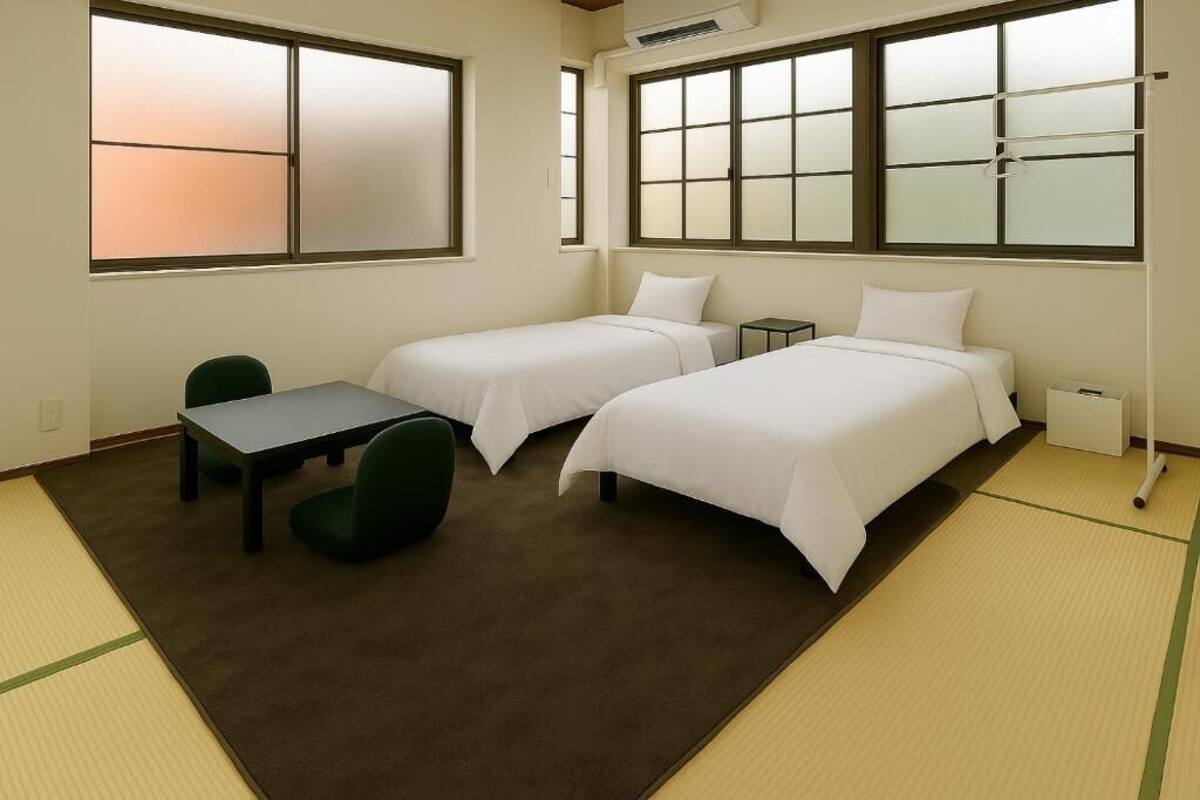 Ein Hotelzimmer mit zwei Einzelbetten, einem kleinen Tisch, einem Stuhl und einer Futonliege.