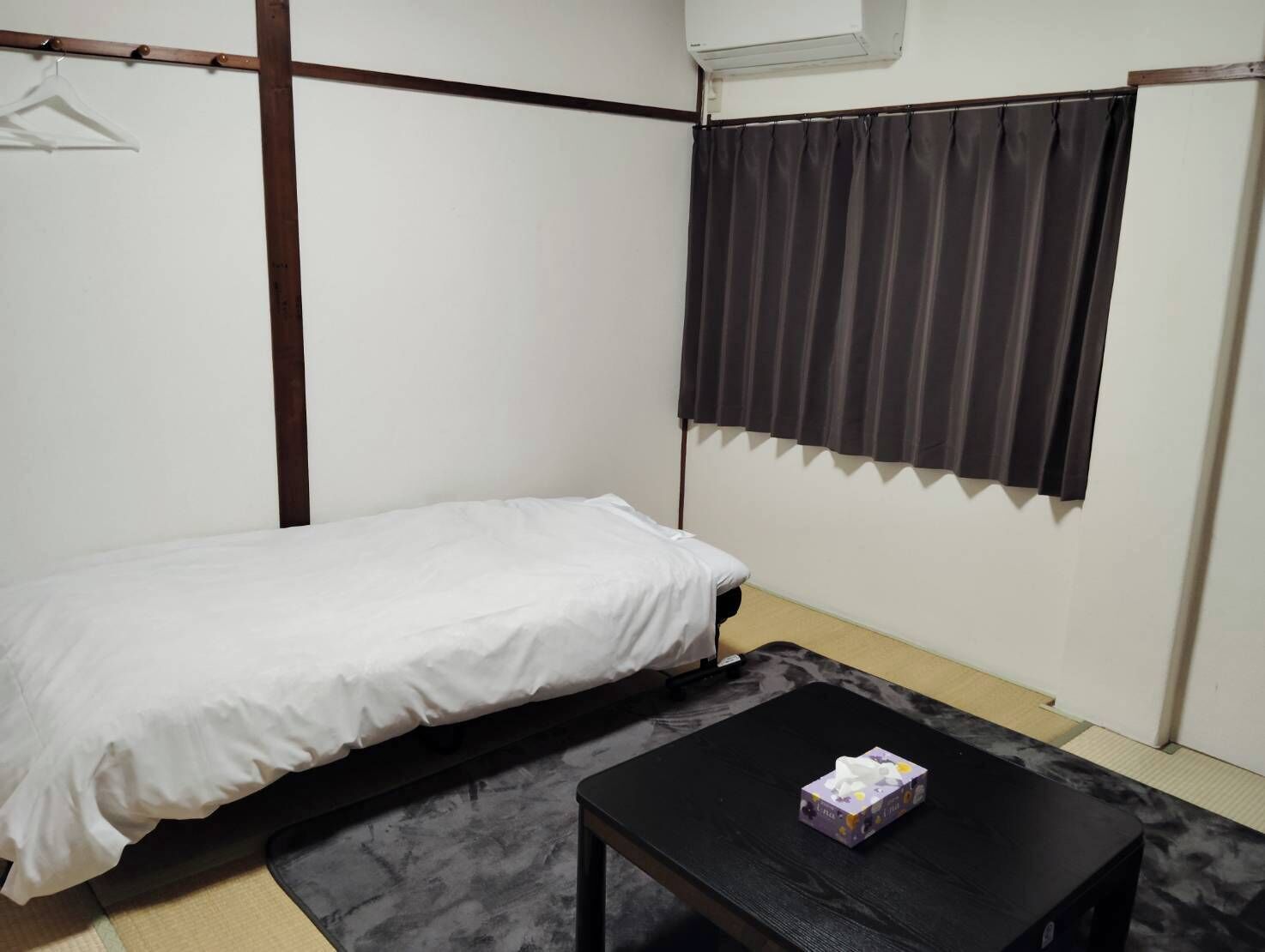 A small, single-bed room with a black table and a hanging garment rack.