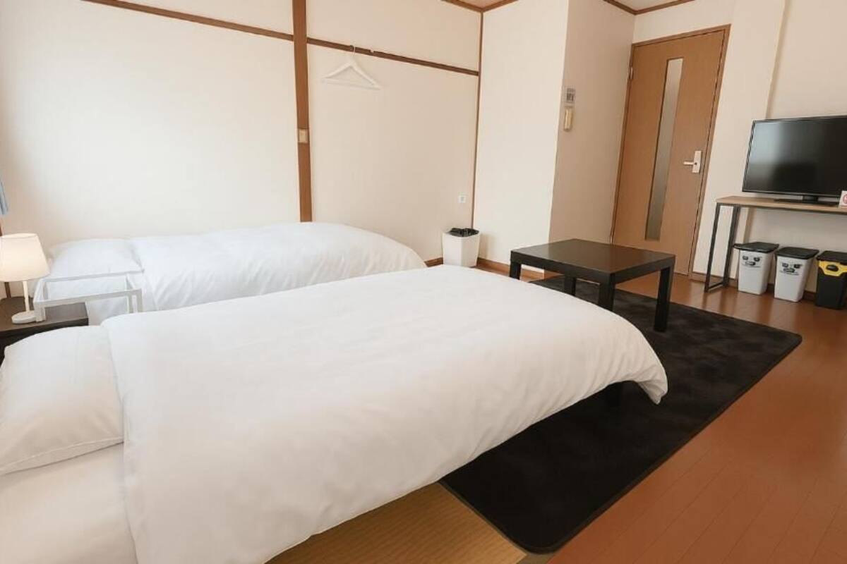 Ein Hotelzimmer mit zwei Betten, einem Schreibtisch, einem Fernseher und einer Mülltonne.