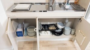 Una cocina con microondas integrado, hervidor de agua y cafetera. Hay dos estantes con platos, tazones y utensilios.