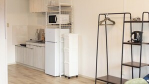 Cocina compacta con armarios blancos, un microondas, un refrigerador y un estante negro suspendido con una tetera.