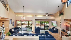 A spacious living area with dark blue sofas, a ceiling fan, and a large sliding glass door leading to an outdoor patio. - Waterfront Clubhouse at Antelope Hills (Prescott)