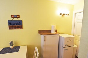 A compact kitchenette with a refrigerator, a small countertop, and a wall-mounted light fixture.
