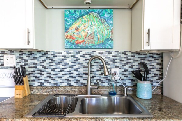 A kitchen with a stainless steel sink, a knife block, and a mosaic backsplash. - Southern PAG Beach House Bungalows (St. Pete Beach)