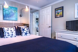 A bedroom with a bed, pillows, a painting, a television, and a door leading to a bathroom. - Southern PAG Beach House Bungalows (St. Pete Beach)