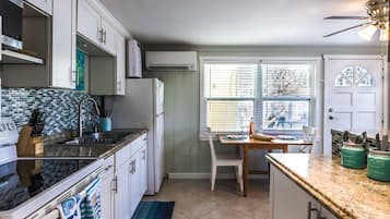 A kitchen with white cabinets, a black countertop, and a window with blinds.
