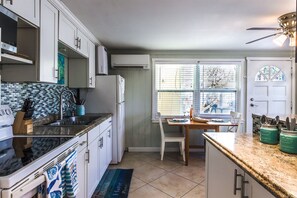 A kitchen with white cabinets, a black countertop, and a window with blinds. - Southern PAG Beach House Bungalows (St. Pete Beach)