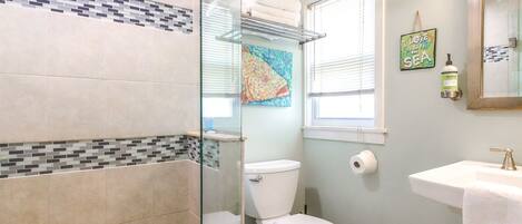A bathroom with a glass shower enclosure, a toilet, a sink, and a towel rack.