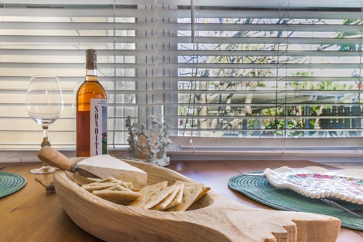 A table with a bottle, a glass, a wooden bowl with cheese and crackers, and a decorative item.