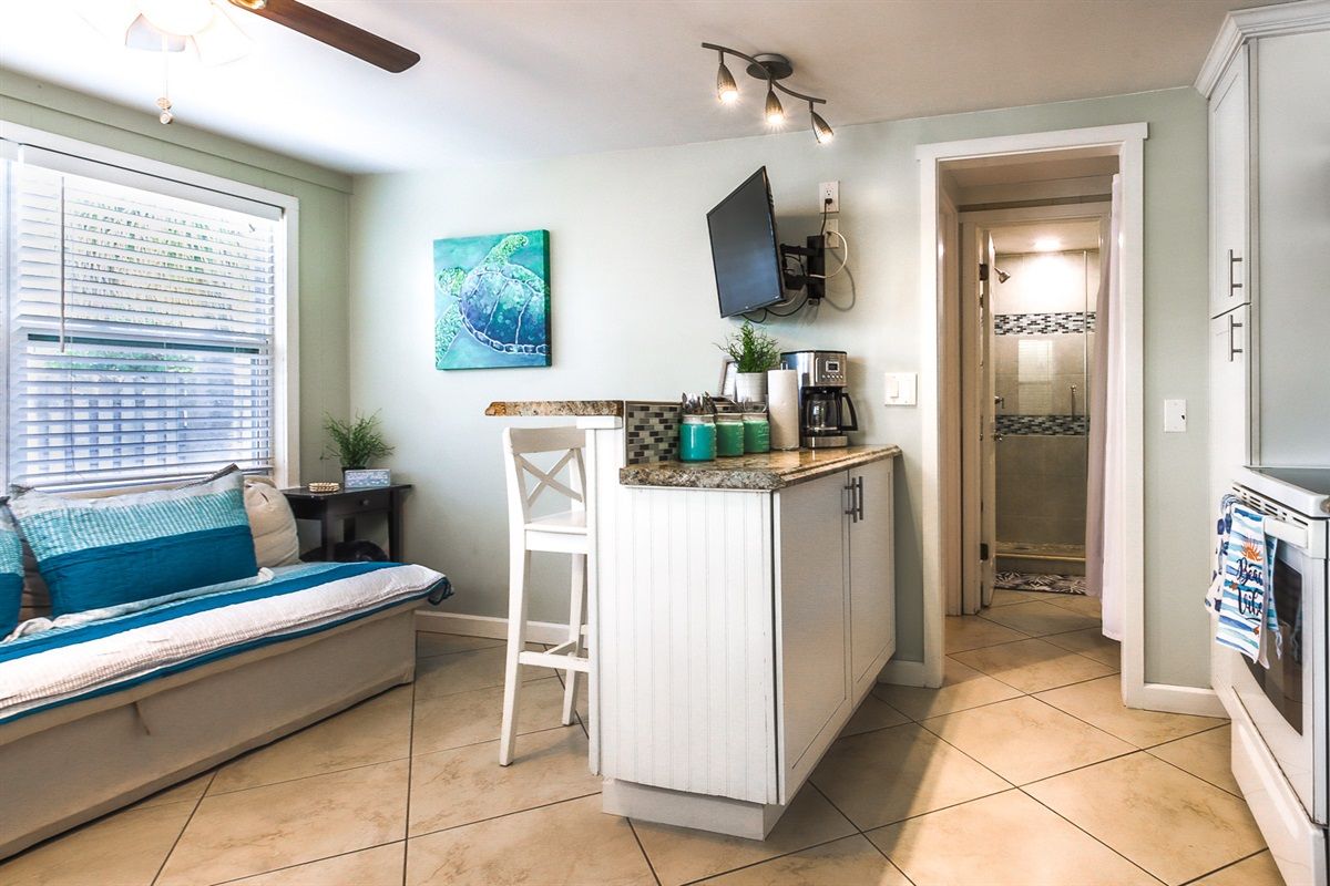 A compact kitchen with a small island, a dining area with a bench, and a view into the adjacent bathroom.