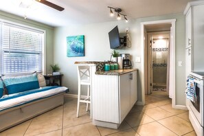 A compact kitchen with a small island, a dining area with a bench, and a view into the adjacent bathroom. - Southern PAG Beach House Bungalows (St. Pete Beach)