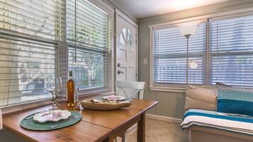 Una habitación acogedora con una mesa de madera lista para comer, un banco con cojines y una puerta con un ventanal.