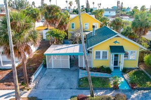 A yellow house with a blue roof, surrounded by palm trees and a white fence. - Southern PAG Beach House Bungalows (St. Pete Beach)