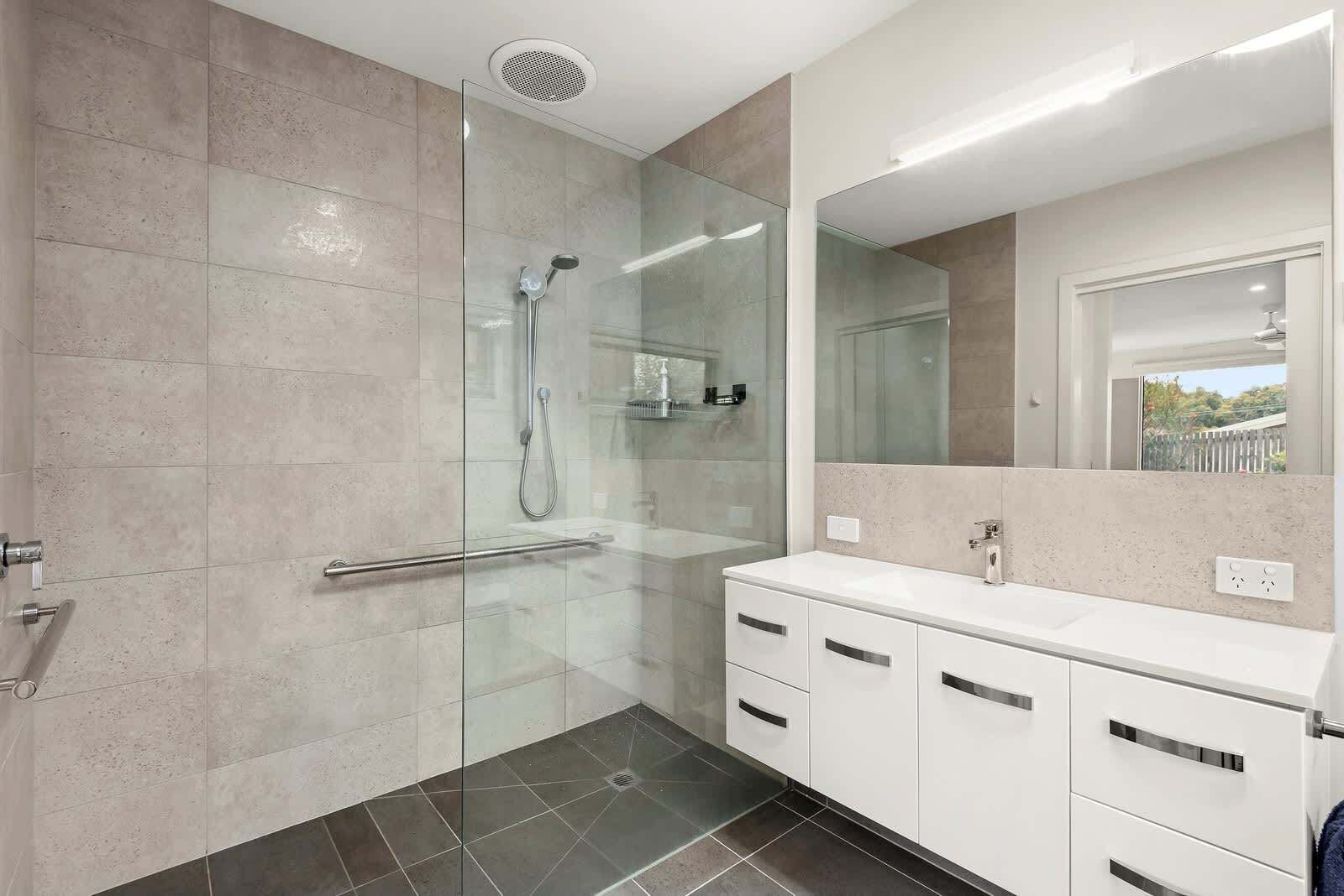 A modern bathroom with a glass shower enclosure, a white vanity with a mirror, and a tiled floor.