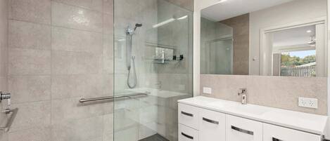 A modern bathroom with a glass shower enclosure, a white vanity with a mirror, and a tiled floor.