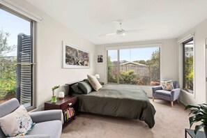 Ein Schlafzimmer mit einem großen Bett, einem grauen Sofa, einem kleinen Sessel, einem Bücherregal und einem Deckenventilator.