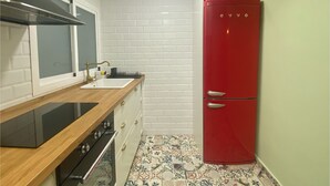 Eine kleine Küche mit einem roten Kühlschrank, weißen Fliesen an der Spritzschutzwand und einer Holz Arbeitsplatte.