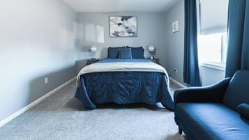Quarto com cama, duas mesas de cabeceira, janela com cortinas e um sofá azul.