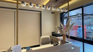 Un comptoir d’accueil avec une pancarte indiquant « RÉCEPTION » et une vue sur l’extérieur grâce à de grandes fenêtres.