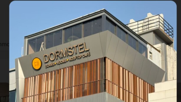 Un bâtiment moderne, reconnaissable à son enseigne « Dormstel », qui propose un café sur le toit, des dortoirs, des chambres et un salon.