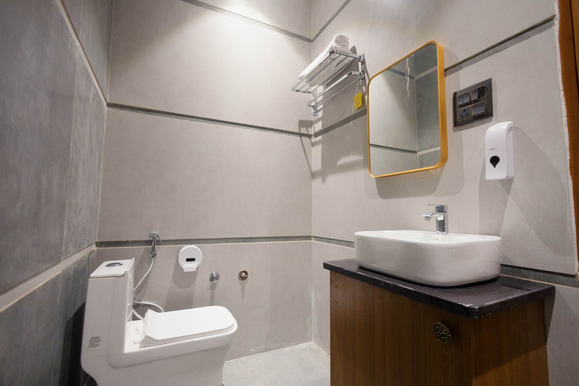 A modern bathroom with a toilet, sink, mirror, towel rack, and hand dryer.