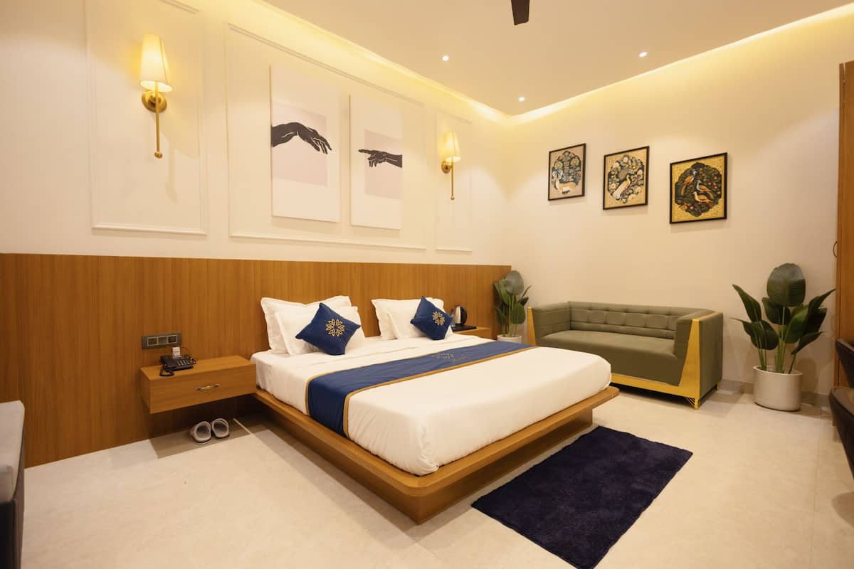 A modern bedroom with a wooden headboard, a large bed with white bedding and blue accents, a green sofa, and artwork on the walls.