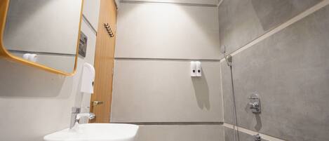 A modern bathroom with a white sink, a mirror, a shower, and a towel dispenser.