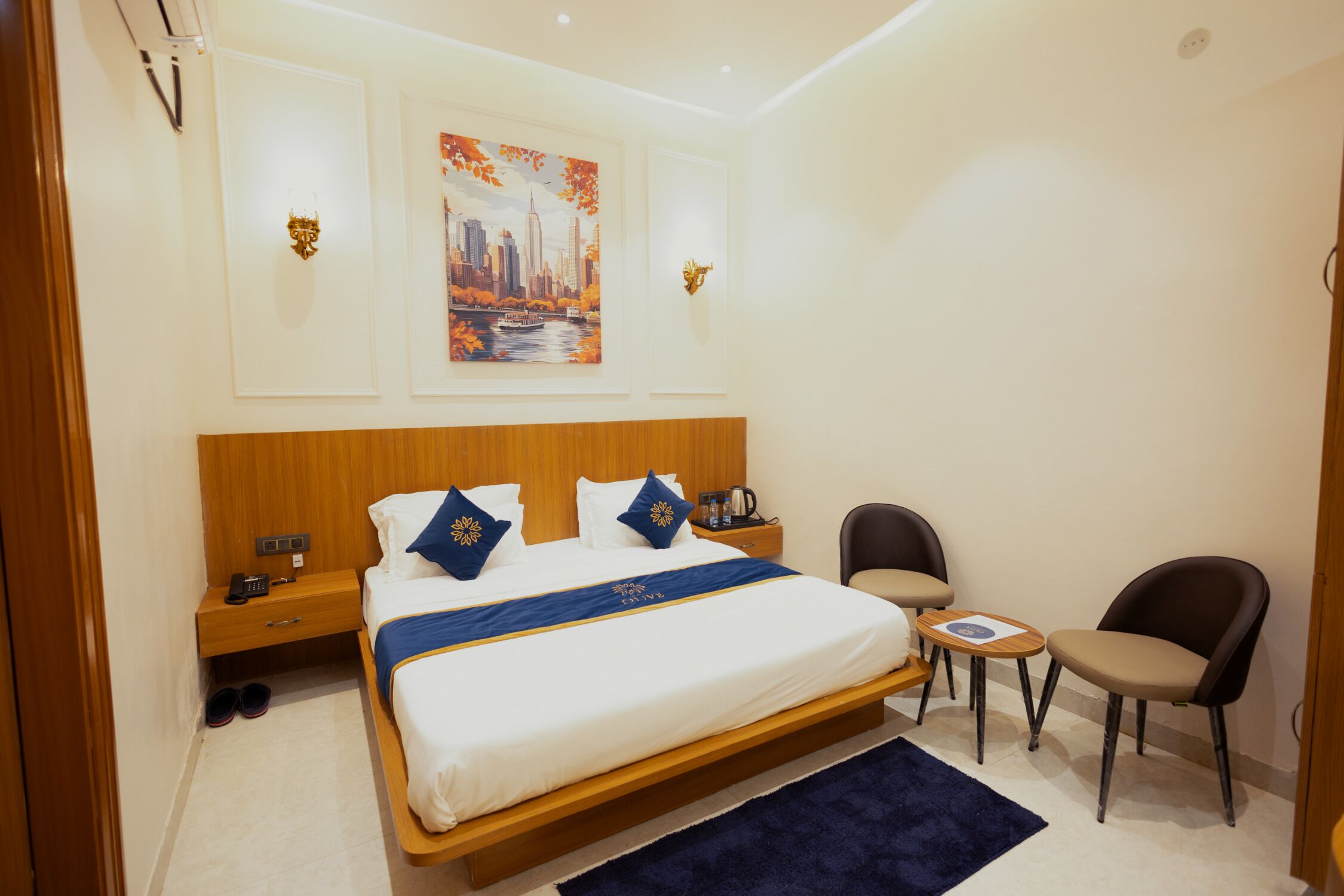 Ein Hotelzimmer mit einem großen Bett, einem kleinen Tisch, zwei Stühlen, einem Nachttisch und einem Bild an der Wand.