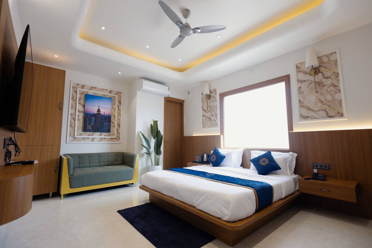 A modern hotel room with a large bed, a ceiling fan, a TV, and artwork on the walls.