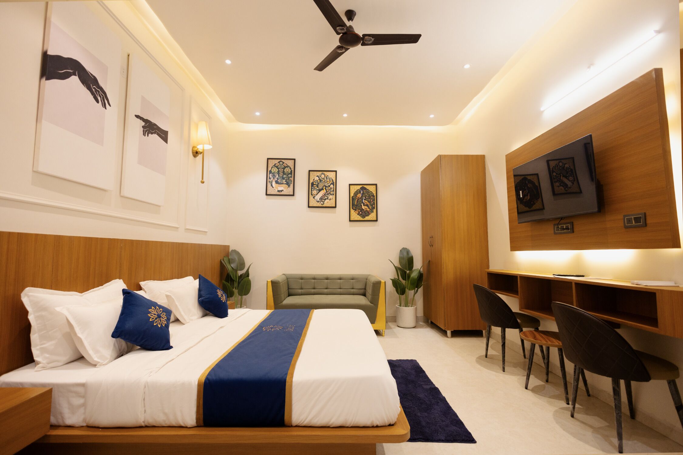 A modern hotel room with a bed, desk, chairs, artwork, and a ceiling fan.