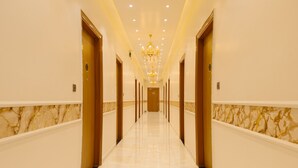 Un largo pasillo bien iluminado con paredes de mármol y puertas de madera, que conduce a una habitación.
