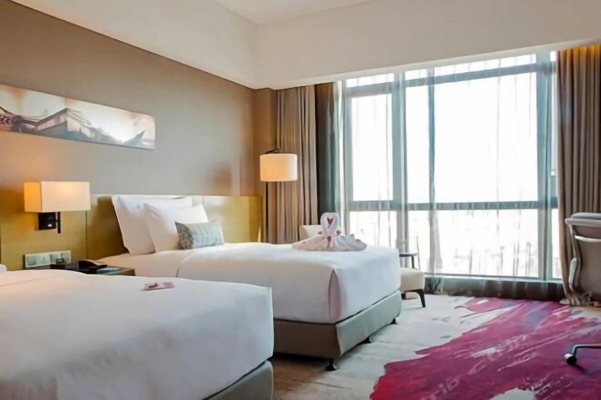 A hotel room with two beds, a large window, and a red carpet.