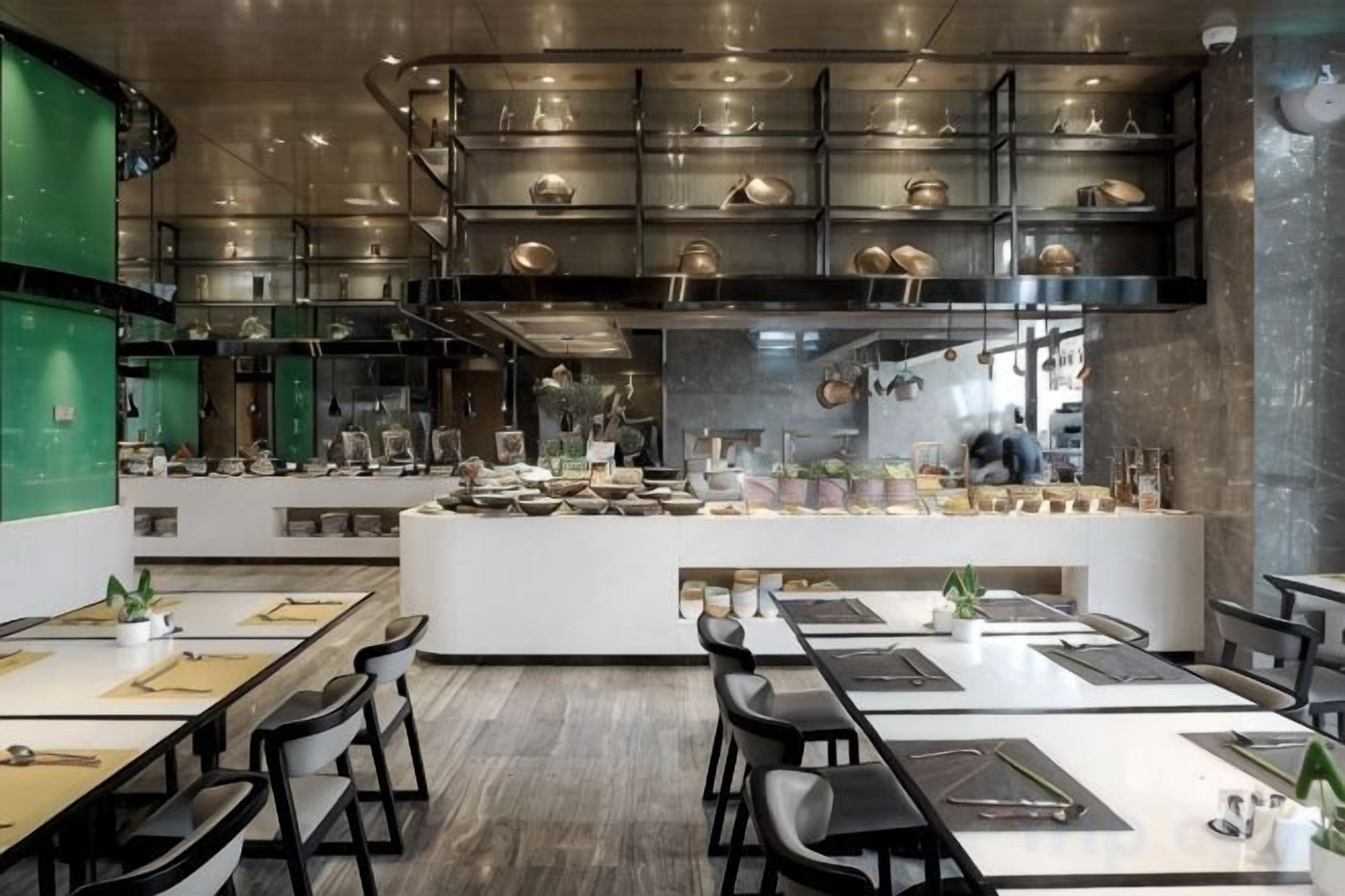Un interior de restaurante moderno con una isla central, varias zonas de estar y una cocina visible al fondo.