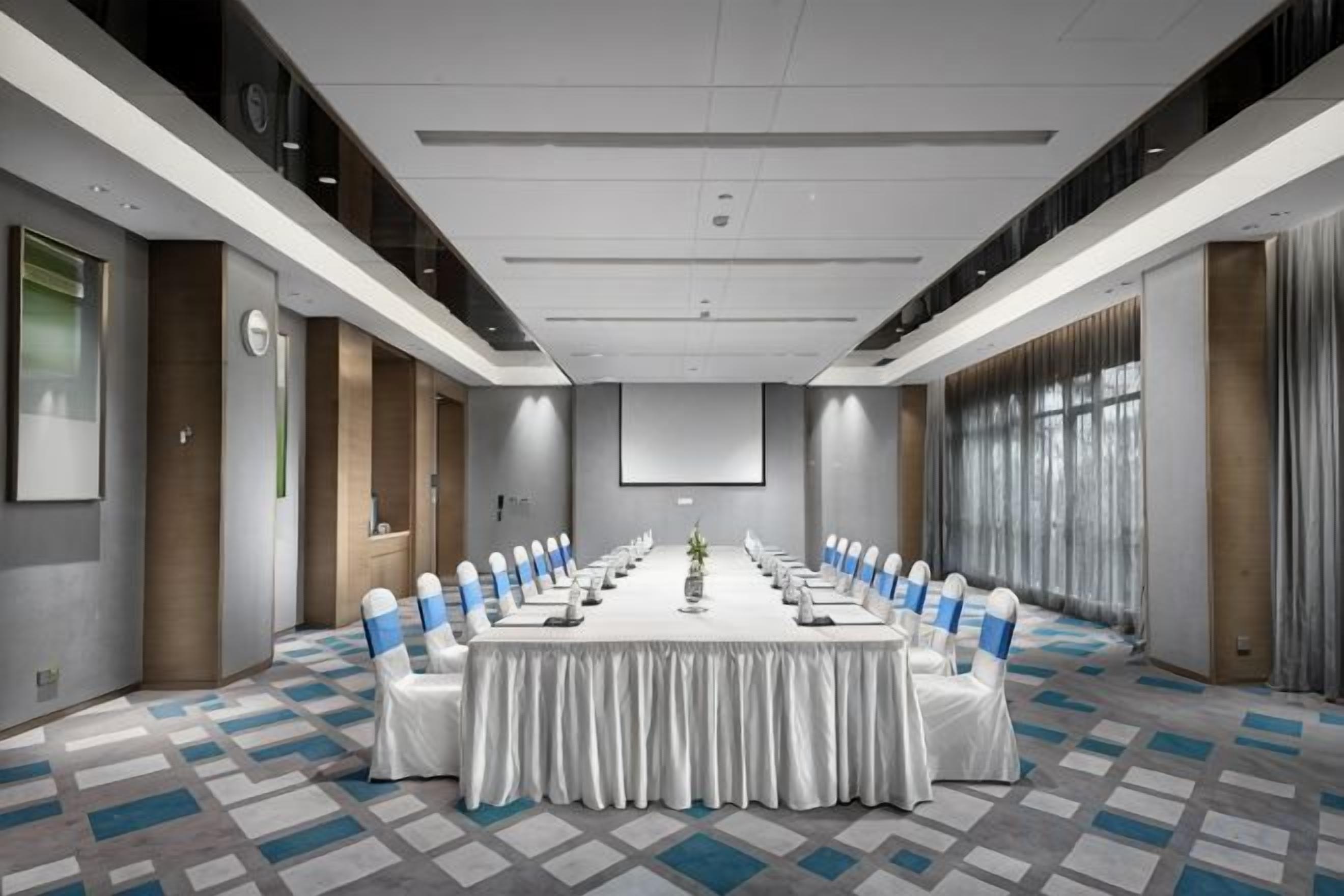 Una sala de conferencias con una larga mesa, sillas y una pantalla de proyector.