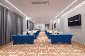 A conference room with rows of tables and chairs, a flat-screen TV on the wall, and a patterned carpet. - Wyndham Jinjiang (Jinjiang)