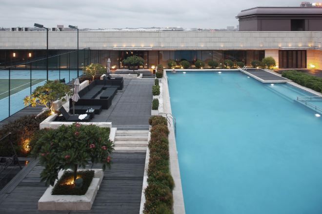 A rooftop pool with a view of a modern building, surrounded by plants and seating areas.