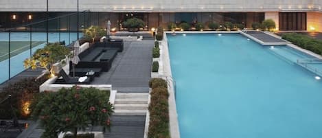 A rooftop pool with a view of a modern building, surrounded by plants and seating areas.