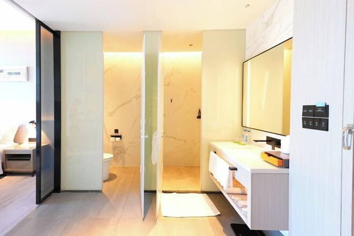 A modern bathroom with a glass partition, a toilet, a sink with a mirror, and a white towel on the floor.