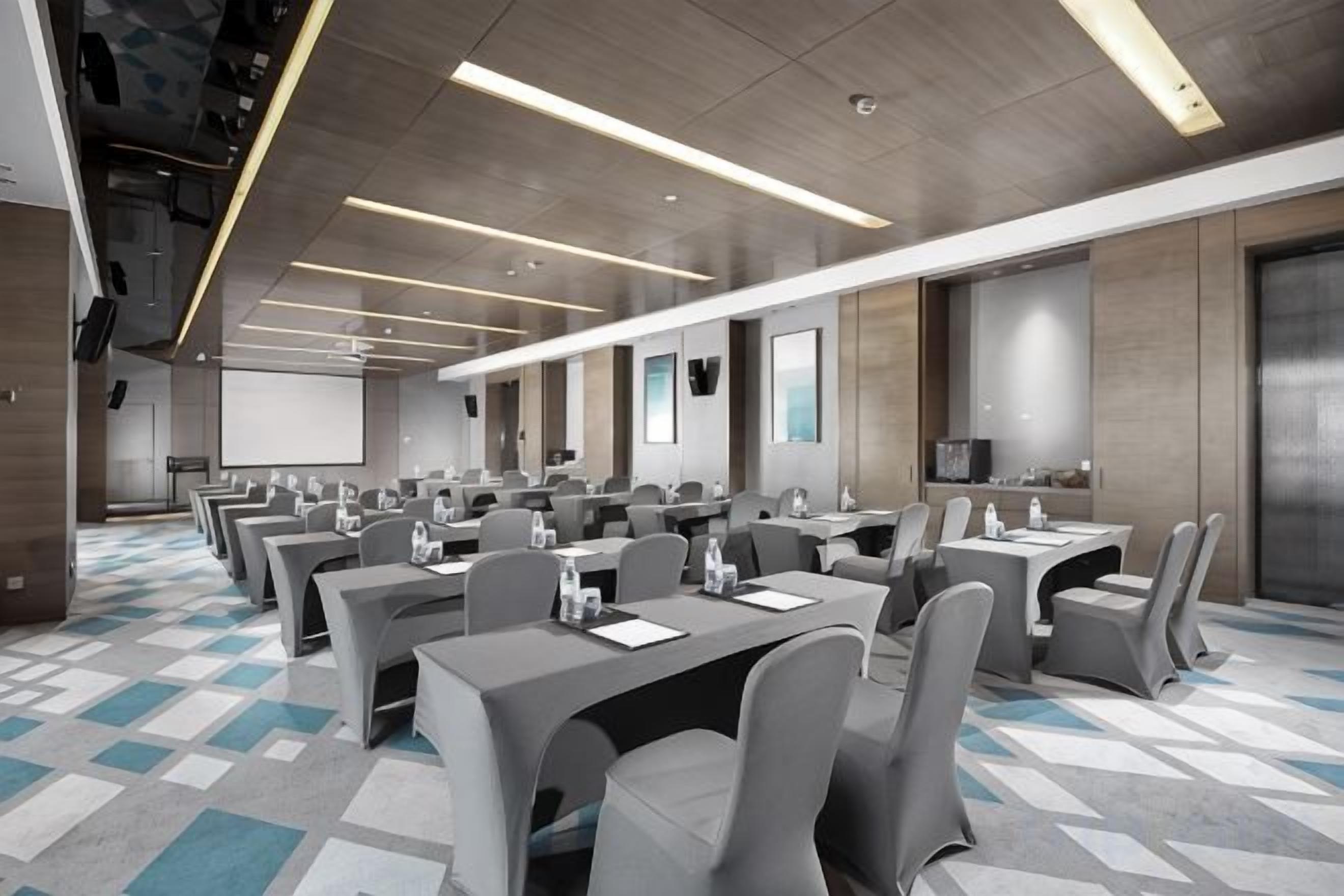 A conference room with multiple tables and chairs, a projector screen, and a large screen on the wall.