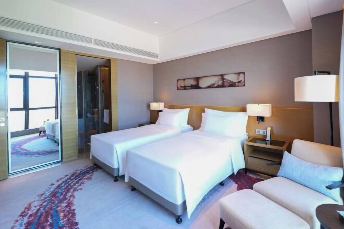 A hotel room with two beds, a sofa, a nightstand, and a large window.