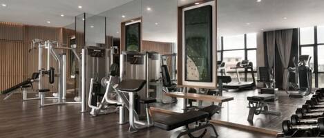 Et moderne fitnesscenter med forskellig træningsudstyr, store spejle og trægulv.