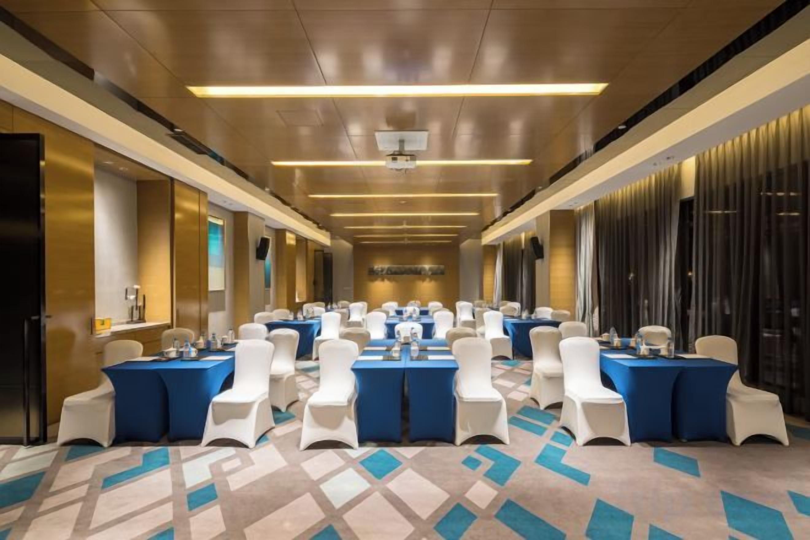 Un salón de conferencias de hotel con varias mesas y sillas, una alfombra estampada y un diseño moderno de techo.
