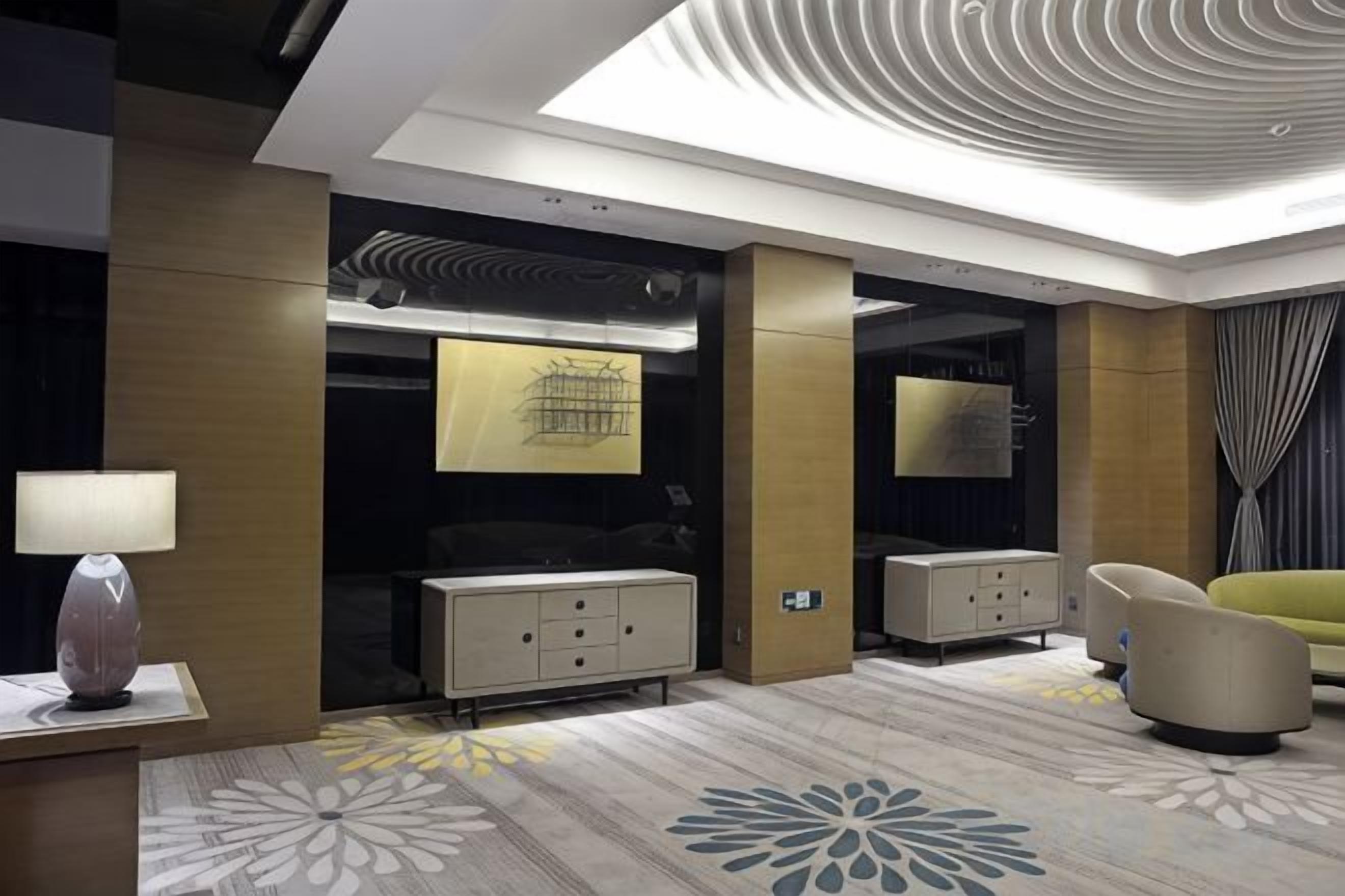 Quarto de hotel com design moderno, apresentando uma cama grande, uma escrivaninha com abajur, um sofá e teto decorativo.