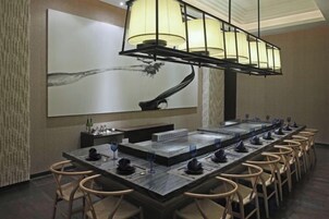 Una larga mesa de comedor con sillas, un cuadro grande en la pared y una lámpara de araña moderna.