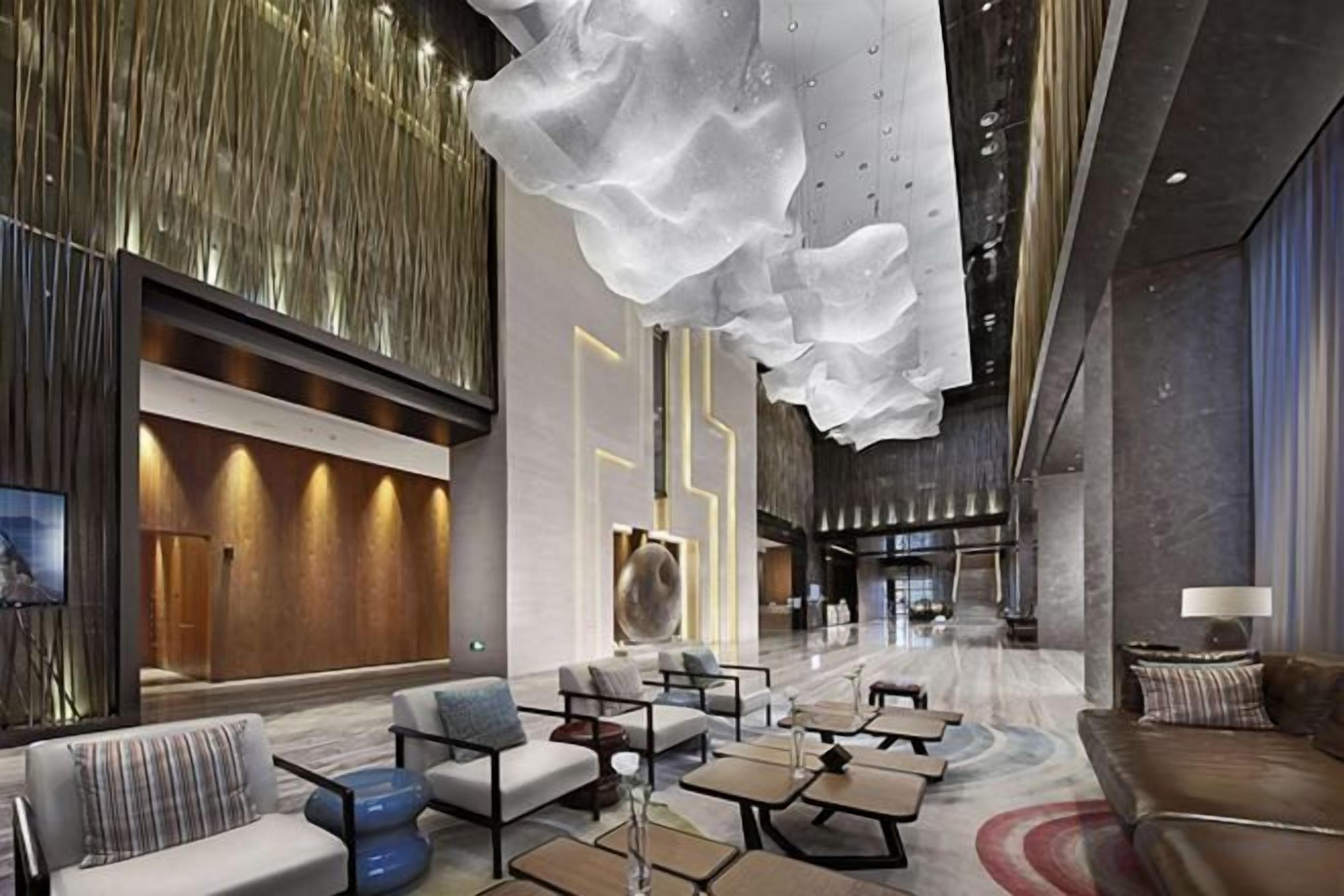 A modern hotel lobby with seating areas, a reception desk, and a large abstract light fixture.