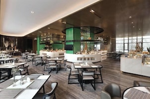 Un restaurante moderno con varias mesas, una pared verde destacada en el centro y una zona de bar.