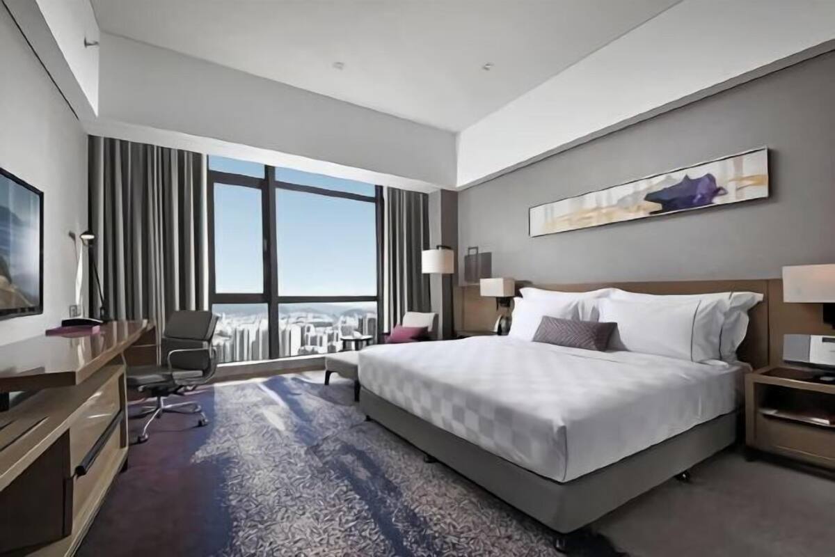 A modern hotel room with a large bed, a desk, and a view of the city.