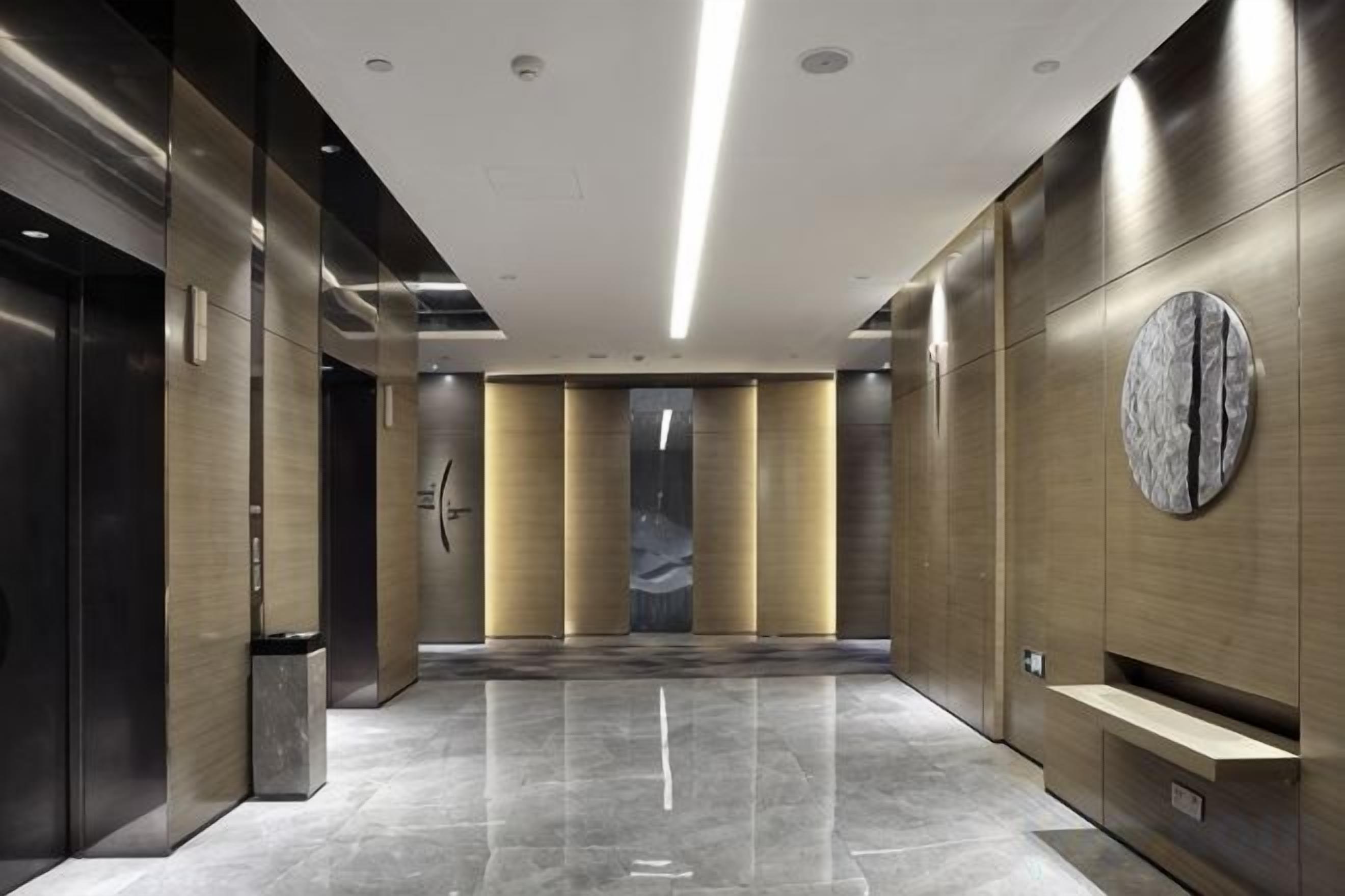 Un vestíbulo de ascensor moderno con piso pulido, paredes metálicas y un adorno circular en la pared.